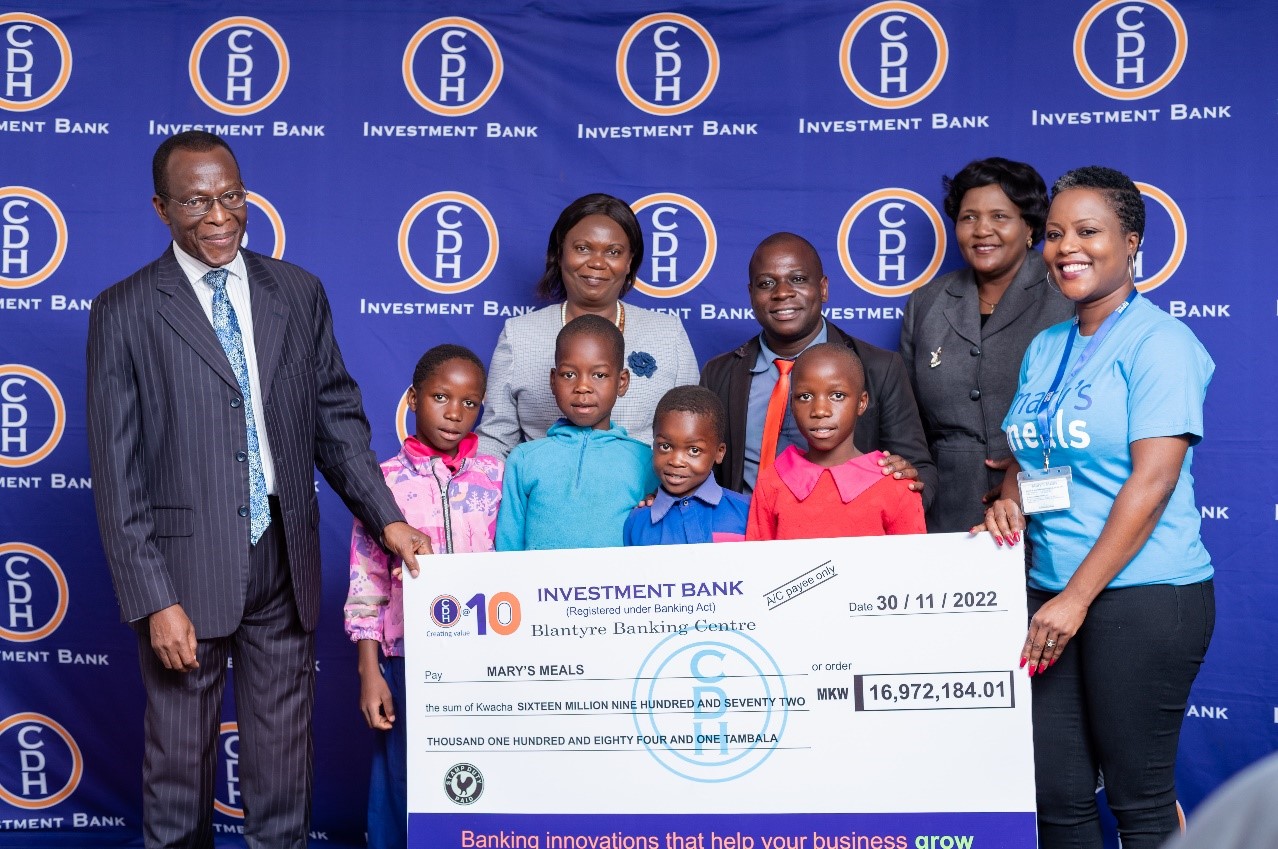 Kwame Ahadzi CDH Investment Bank Chief Executive Officer (L) hands over symbolic cheque to Angela Chipeta Khonje Mary’s Meals Country Director, flanked by representatives from Ministry of Education, Mbinda Junior Primary School Head Teacher and children of Mbinda junior Primary School 
